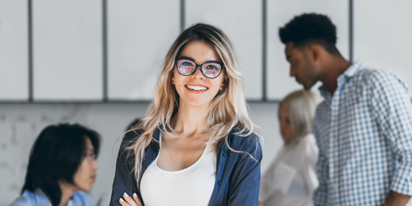 Confident Blonde Female Manager Posing With Smile After Conference With Other Employees Asian Programmer Talking With African Freelancer While Fair Haired Secretary Laughing (1)